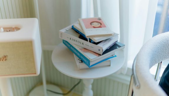 Books are stacked on a small white table.